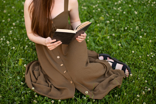girl in olive dress reading a book while sitting on green grass