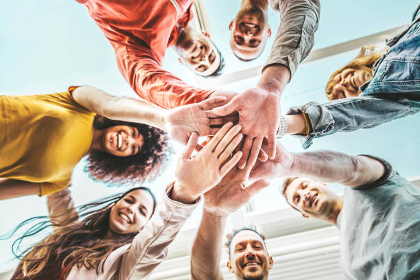 Group of young people stacking hands together outdoor - Community of multiracial international people supporting each other - Union, support and human resources concept stock photo