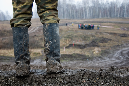 The man stand  in muddy kersey boots.