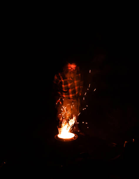 istock a man putting wood into a fire pit at night 1402689393