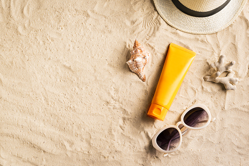 Sunscreen lotion on sandy beach as background, top view, copy space. Summer vacation and skin care concept, spf uv-protect cosmetic products.