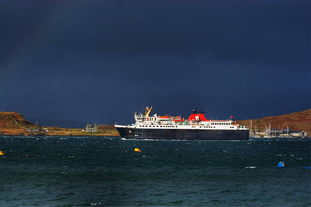Ferry in Storm A Hebridean ferry caught against black clouds in a shaft of sunlight during a storm with the Island of Kerrea in the background.  oban stock pictures, royalty-free photos & images