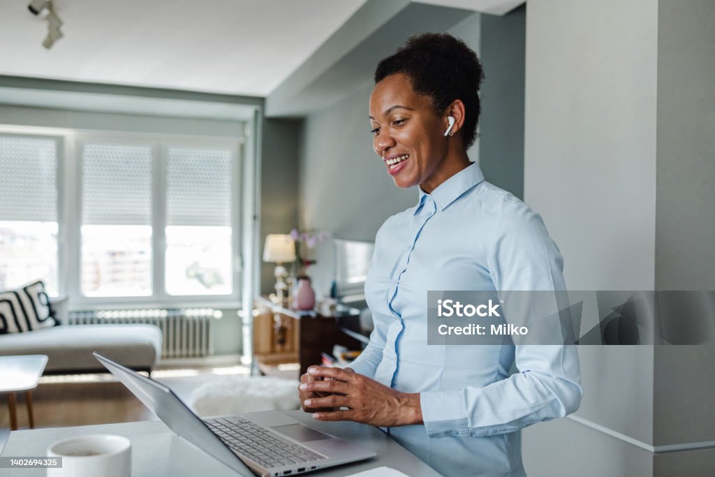 Video call communication and working from home African-American woman talking with co-workers on a video call Wireless Headphones Stock Photo