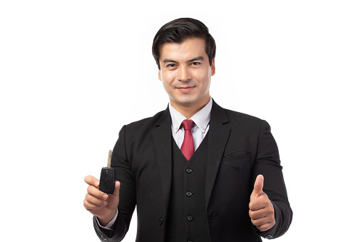 Portrait of a confident business man in black suit feeling happy and smile holding the keys of the car isolated on white background.