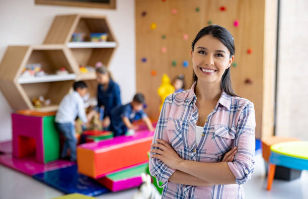 Happy elementary school teacher smiling in the classroom Portrait of a happy Latin American elementary school teacher smiling in the classroom and looking at the camera preschool teacher stock pictures, royalty-free photos & images