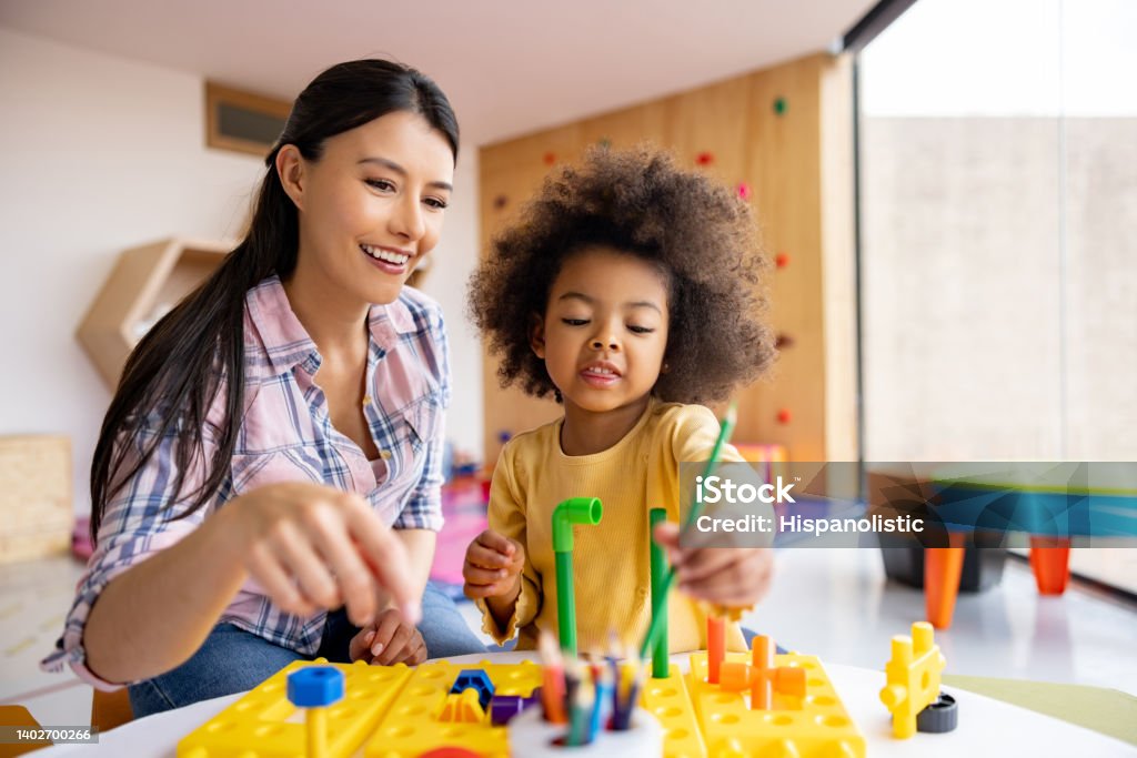 Happy teacher playing with a girl in the classroom Happy Latin American teacher playing with an African American girl in the classroom Learning Stock Photo