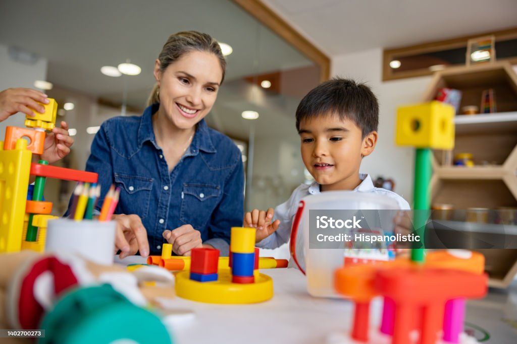 Schoolboy playing with building blocks in the classroom Happy Latin American schoolboy playing with building blocks in the classroom and the supervision of his teacher Occupational Therapy Stock Photo