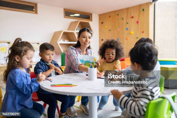 Group Of Children Coloring In Art Class With The Supervision Of Their Teacher Stock Photo - Download Image Now