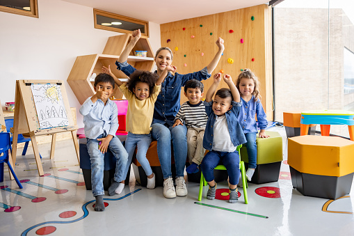 Small nursery school children with teacher sitting on floor having lesson. Young woman teach preschool kids in classroom sitting on floor together