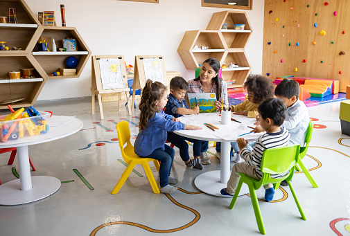 Arts teacher supervising a group of students coloring in class at an elementary school - education concepts