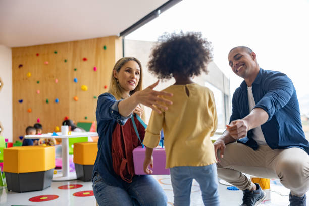 glückliche eltern, die ihre tochter begrüßen, während sie sie von der schule abholen - preschool father offspring child stock-fotos und bilder