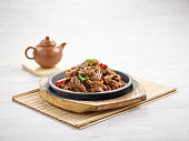 Hot-Plate Mutton with Cumin in a dish isolated on wooden board side view on grey background