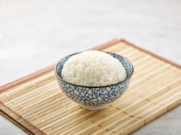 fragrant rice ina bowl isolated on wooden mat side view on grey background fragrant rice ina bowl isolated on wooden mat side view on grey background jasmine rice stock pictures, royalty-free photos & images