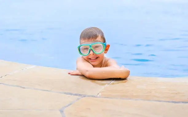 Photo of Little smiling boy in swimming goggles in the outdoor pool.