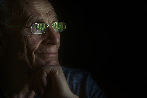 Mature male person wearing eyeglasses looking through window sitting indoor isolated on black background