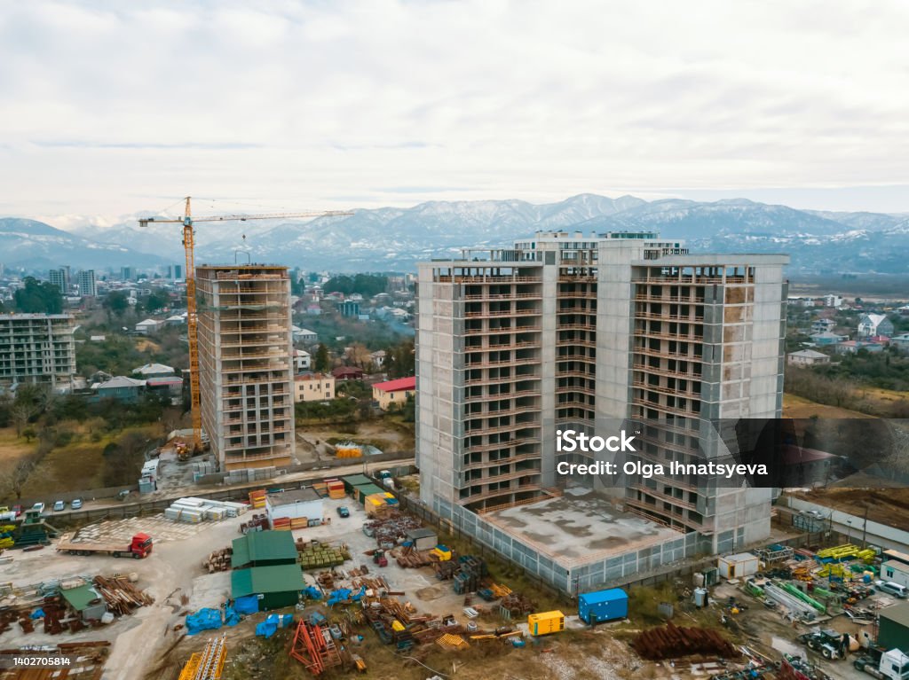 Drone view of the construction site, multi-storey buildings under construction against the background of mountains. Construction machinery, excavators, tractor crane Aerial View Stock Photo