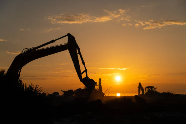 silhouette eines großen raupenbaggers, der auf dem meeresdamm vor dem hintergrund eines atemberaubenden sonnenuntergangs arbeitet. graben des bodens für das fundament und den bau eines neuen gebäudes. - ajaria stock-fotos und bilder