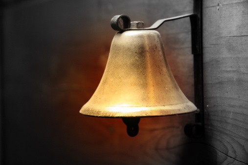 suspended bell, a photograph that could be used for the holidays. the bell is held by a hanger which is connected to a wooden wall.