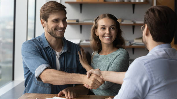 istock Happy couple clients handshake relator at meeting 1402711490