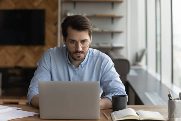 istock Serious man look at laptop screen work online at workplace 1402711552