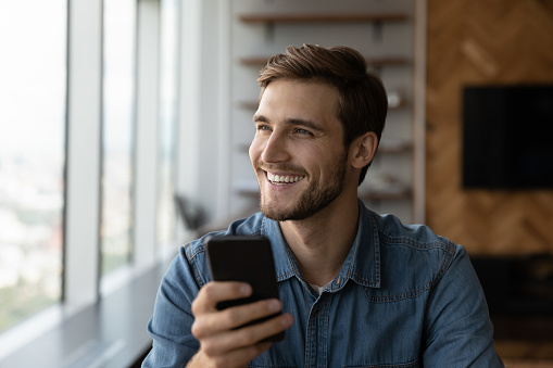 Overjoyed millennial Caucasian man use cellphone talk speak on video call on modern gadget. Smiling young male look in distance hold smartphone have webcam virtual communication. Technology concept.