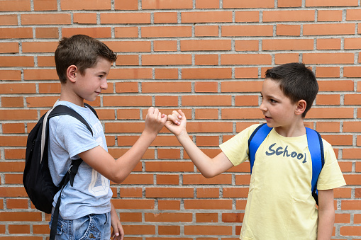 Two schoolchildren greet each other by linking fingers. Back to school concept
