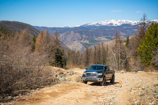 Aktash, Russia - May 9, 2022: Car on road uphill with large stones in the background of the forest and mountains, off-road in Altai, Russia. High quality photo