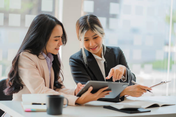 istock Two Asian business women working together using digital tablets discussing new startup project ideas. Analyze the planning and statistics of the financial and investment markets at the office. 1402715688