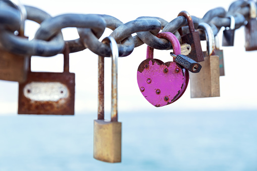 Close up of different colorful love locks on rusty chain on blurred sea background. Selective focus. Romantic concept.