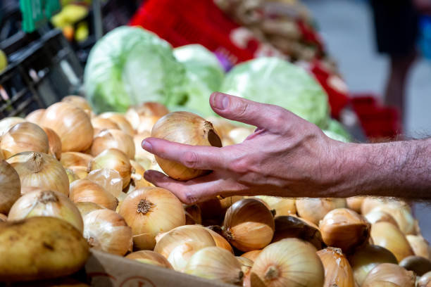 A man choosing an onion from a display in a supermarket, with a shallow depth of field