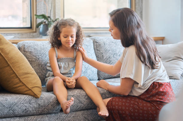 menina triste sentada no sofá enquanto a mãe tenta falar com ela. mãe carinhosa tentando se comunicar com a filha chateada. jovem mãe hispânica perguntando a menina o que está errado ao tentar confortá-la e mostrar apoio - parent - fotografias e filmes do acervo