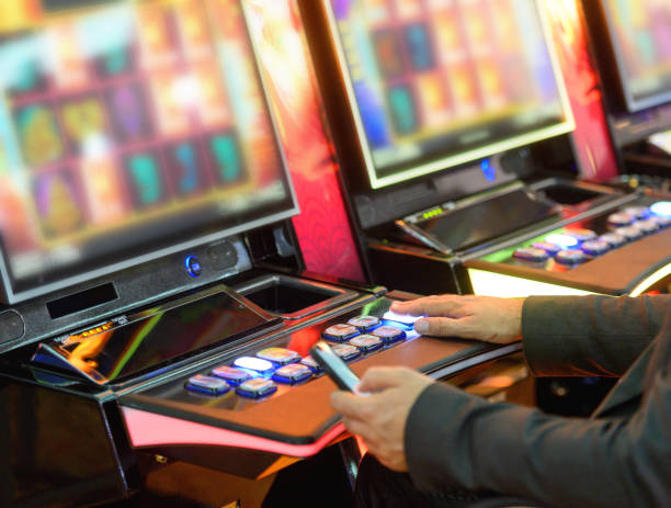 Playing on slot machines Unrecognizable man sitting and playing on slot machines, holding smart phone in other hand slot online stock pictures, royalty-free photos & images