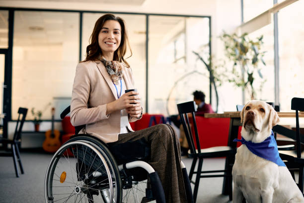 feliz mujer de negocios en silla de ruedas con perro de asistencia en la oficina. - service dog fotografías e imágenes de stock