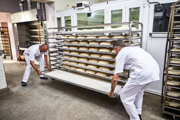 istock Professional bakers in uniform inserts cart with decks for baking raw dough to make bread in an industrial oven in a bakery 1402731228