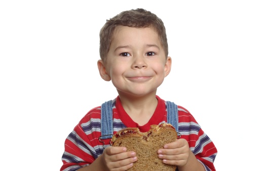 A five-year-old boy holds a whole-wheat peanut butter and jelly sandwich with a bite taken out of it, isolated on white background