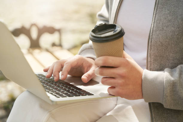 mãos masculinas segurando xícara de café e amarrando no teclado do laptop - human hand computer keyboard male netbook - fotografias e filmes do acervo