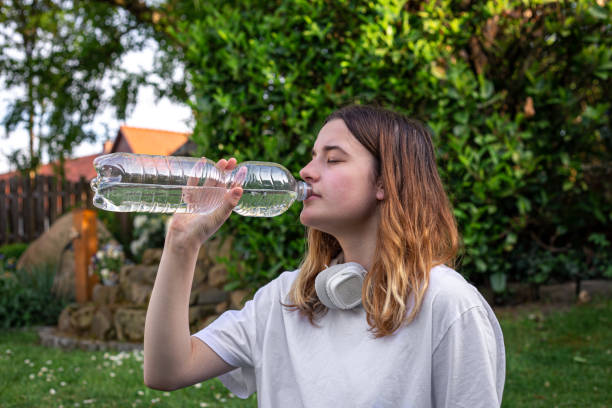 A young woman on a mat drinking water from a bottle in nature. A young woman on a mat drinking water from a bottle in nature, the concept of playing sports, training and fitness. Drinking plenty of water stock pictures, royalty-free photos & images