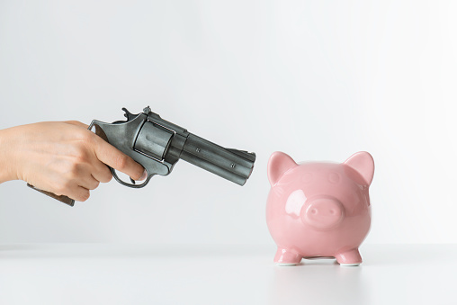 Hand with gun is aiming a pink piggy on white background.