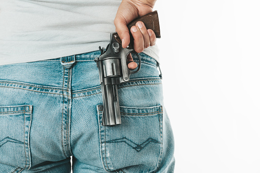 Back view of an unrecognizable person wearing a gray t-shirt and blue jeans which is hiding a gun.