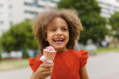 a black laughing child with ice cream in a waffle cone at summer day