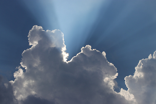 Blue sky background with sun rays behind the clouds and copy space.