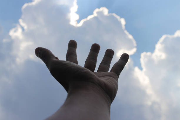 Hand against clear Blue sky background with sun rays behind the clouds.