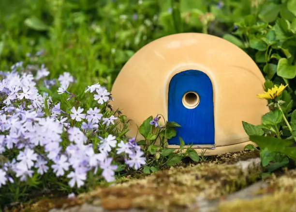 Cute ceramic house with attractive blue door for nesting bumble bees on a spring garden around carpet phlox flowers.  Help people to animals concept.