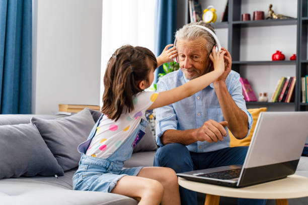 grandchild is making his grandfather listen to music on the computer and they are having fun stock photo