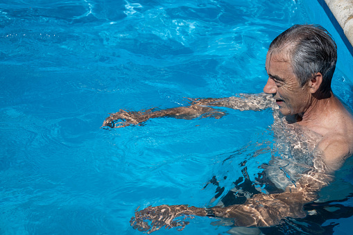 Caucasian mature man in his 60s with white hair exercising in the swimming pool to maintain healthy