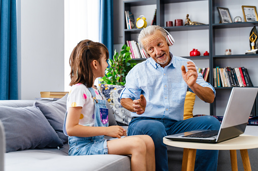 grandchild is making his grandfather listen to music on the computer and they are having fun