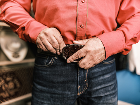 Hands of Mature Latin man getting dressed as Vaquero-Mexican Cowboy. He has  western themed clothes with shirt and jeans. Interior of private home.