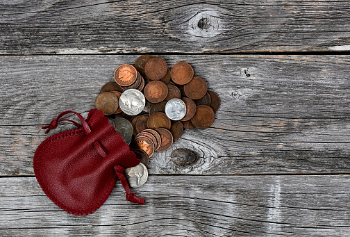 Small red leather bag of United States vintage coins on rustic wood background