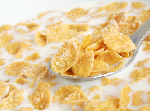 Bowl of corn flakes with milk and a bottle of milk on white background.