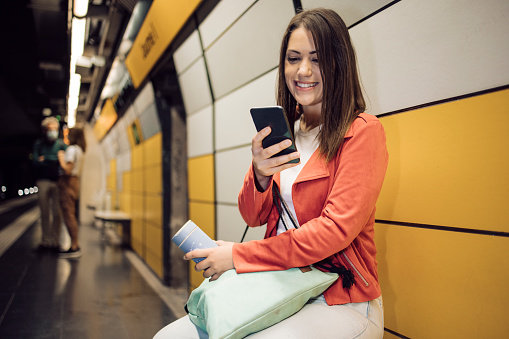 Portrait of a young woman on vacation in Barcelona waiting for his train in the subway and using his smartphone.